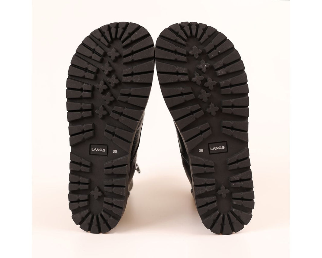 A pair of black boots shown from the sole view, displaying deep lugged rubber tread patterns and the brand name 'LANG.S' printed on the soles, set against a plain off-white background.