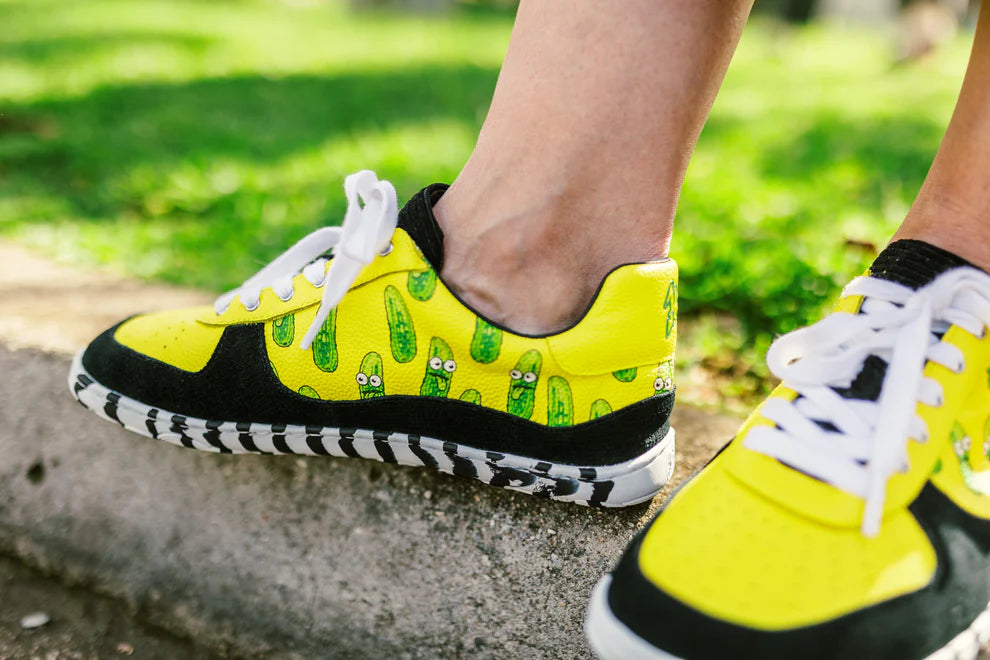 Yellow PaperKrane sneakers with pickle pattern worn outdoors on a concrete surface.