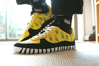 Yellow and black sneakers with green accents worn indoors by PaperKrane