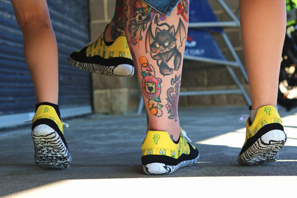 Person wearing yellow PaperKrane Barefoot shoes with black soles, standing on a concrete surface.