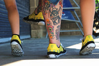 Person wearing yellow PaperKrane Barefoot shoes with black soles, standing on a concrete surface.