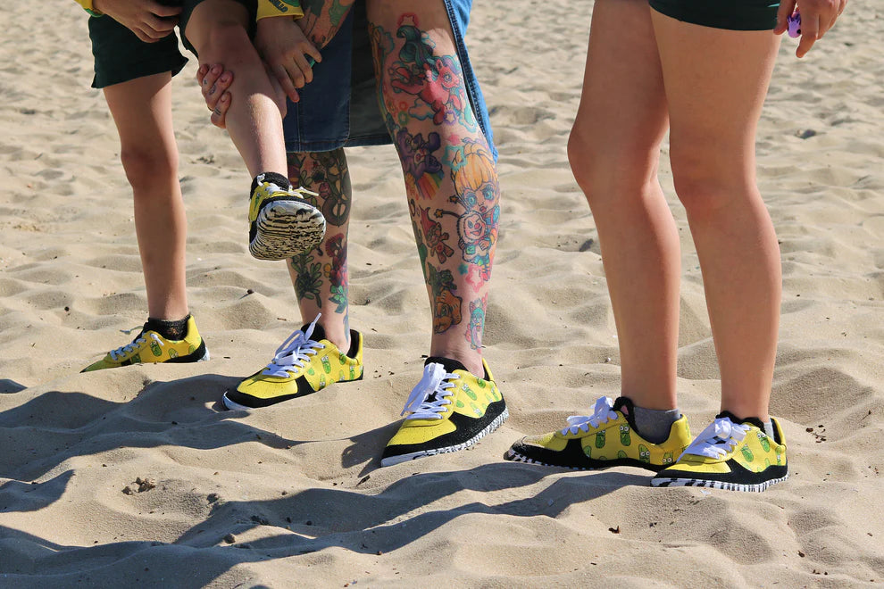 Three pairs of feet wearing barefoot shoes by PaperKrane on a sandy surface.