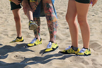 Three pairs of feet wearing barefoot shoes by PaperKrane on a sandy surface.