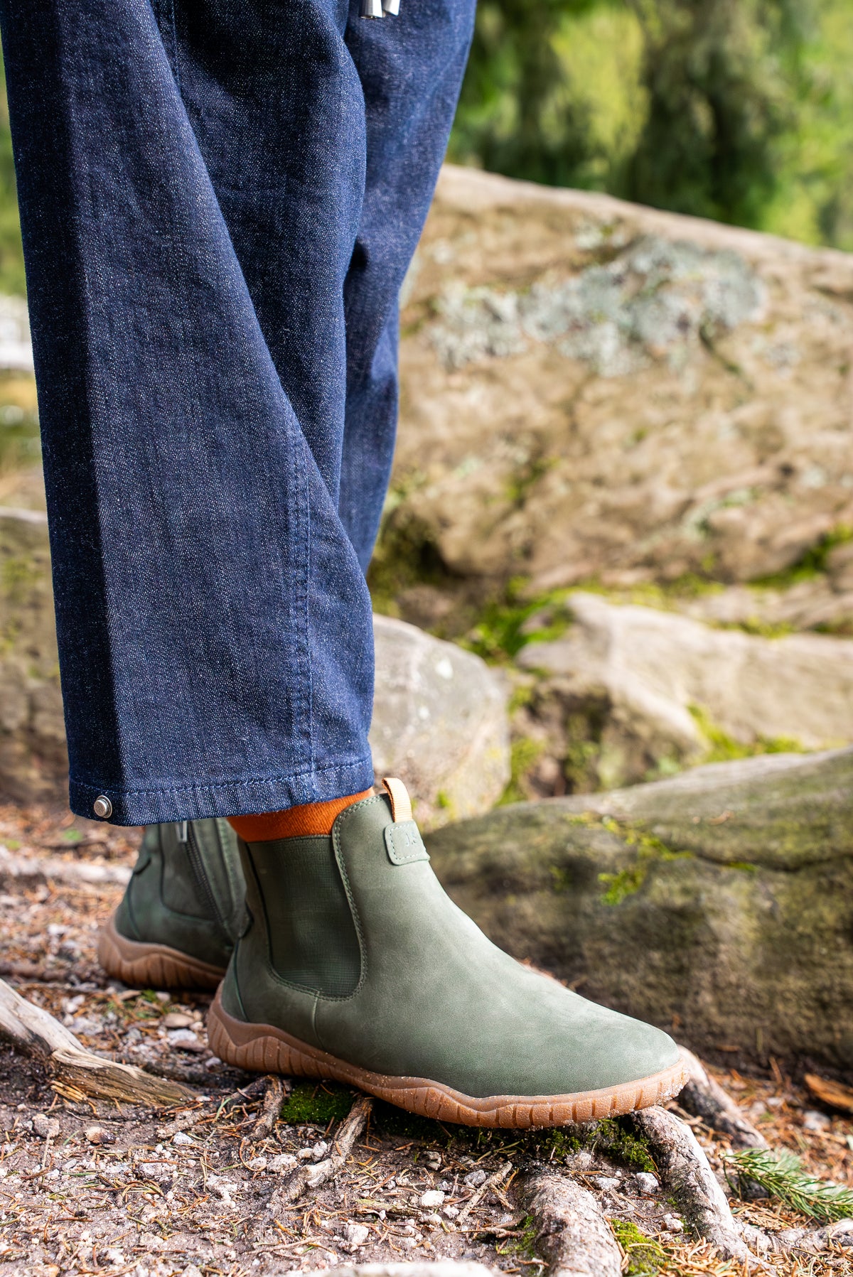 Close-up of indigo jeans and olive green Josef Seibel Chelsea boots on mossy rocks and tree roots