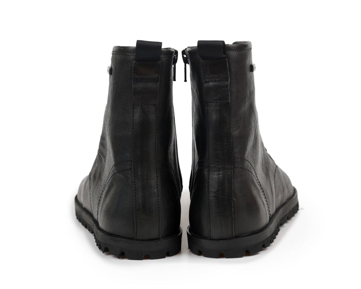 A pair of black leather tikki langs boots shown from the back, featuring side zippers and rugged black soles, set against a plain white background.