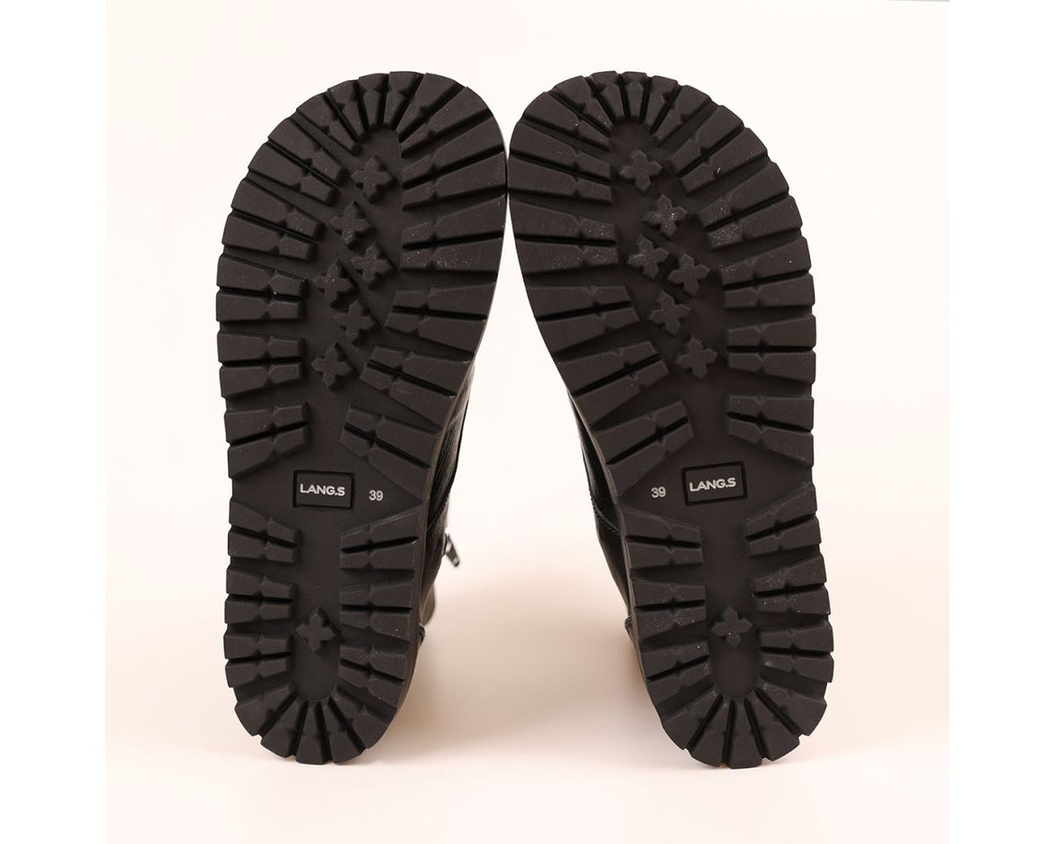 A pair of black boots shown from the sole view, displaying deep lugged rubber tread patterns and the brand name 'LANG.S' printed on the soles, set against a plain off-white background.